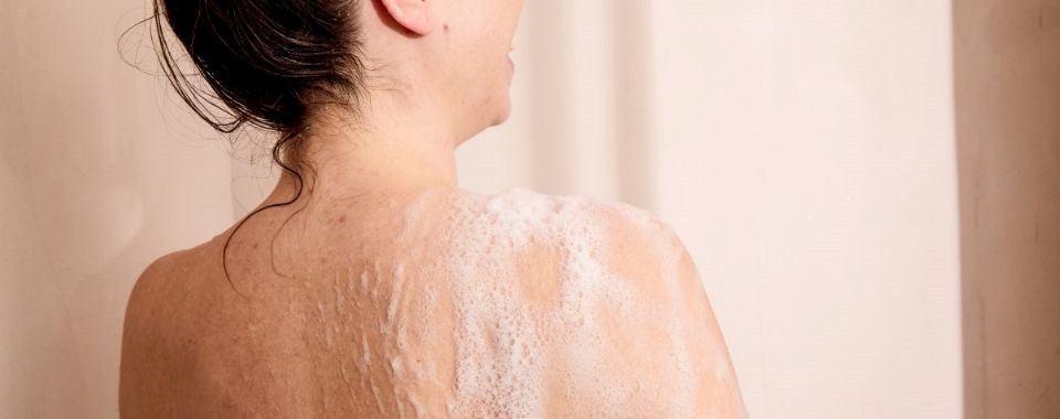 FEMME-SOURIANTE-SOUS-SA-DOUCHE-MOUSSE-SUR-SON-EPAULE